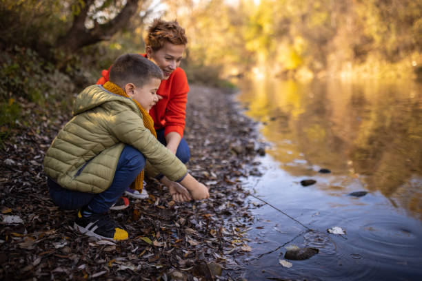 Mother and her little son having fun playing with sticks by the river outdoors in nature.