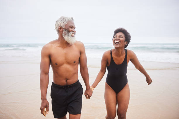 istock Mature couple in swimsuits laughing while walking on a sandy beach 1457955671