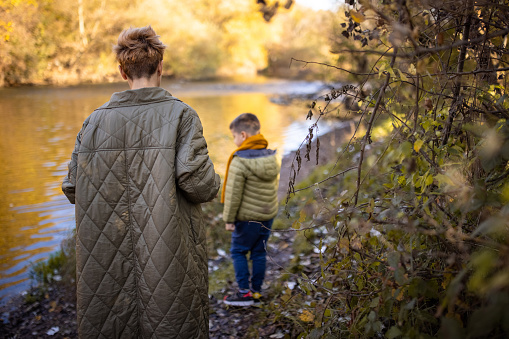 Mother and her little son taking a walk by the river outdoors in nature.