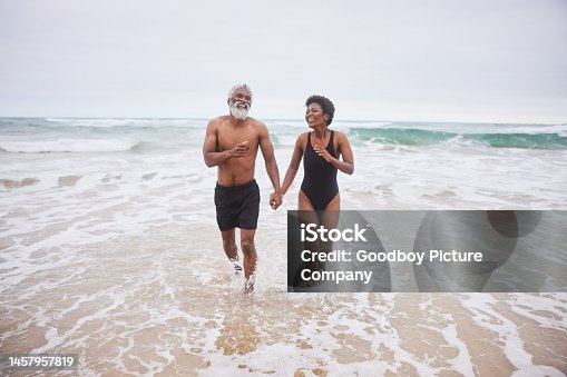 istock Laughing mature couple in swimsuits walking in the ocean 1457957819
