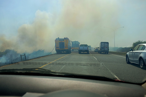 Cape Town, South Africa - January 10, 2023: Traffic is forced to stop as smoke from a bush fire envelopes the N2 highway just inland from Cape Town. Wildfires are common during the region's hot, dry summers. A fire truck is parked beside the road.