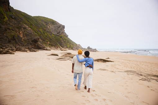 Rear view of a mature couple walking arm in arm together along a sandy beach on an overcast day
