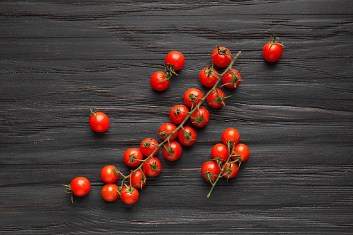 Cherry tomatoes on a branch on a dark wooden background top view. Fresh cherry tomatoes on a wooden background. Healthy food. Veganism.