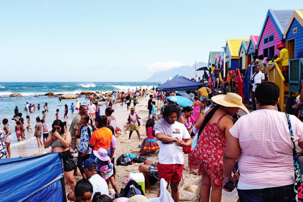 menschenmenge am strand von st. james, mit bunten strandhütten zum umziehen - cape town beach crowd people stock-fotos und bilder