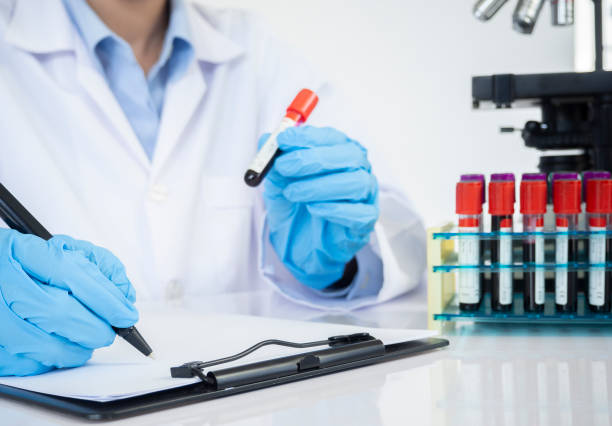 ラボのバックグラウンドで分析の機械とラックから血液サンプルチューブを取る医師の手。 - vial laboratory test tube biotechnology ストックフォトと画像