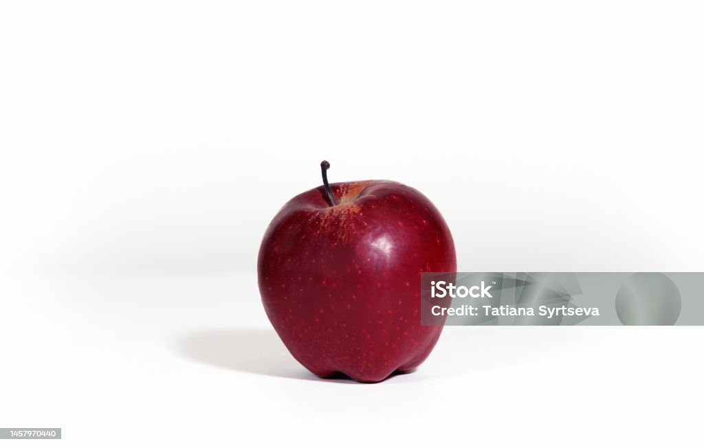 Red ripe apple isolated on white background with hard shadow. An apple is on the table in the kitchen. Apple - Fruit Stock Photo