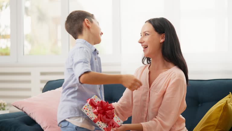 Cute little boy giving present box to his mother, celebrating Mother's day