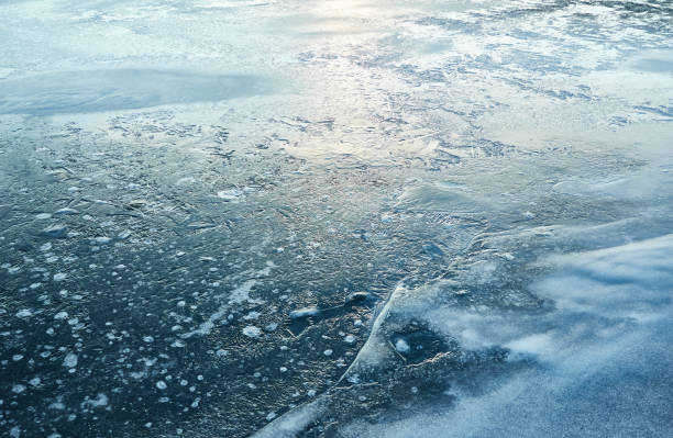 istock Cracked ice, snowflakes, snow, water surface, frozen lake shore. Sunset or sunrise. Texture, close-up. Winter scenery. Concept image, graphic resources. Nature, ecology, climate, global warming 1457972719
