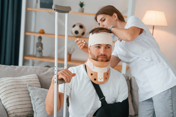 prendre soin du bandage sur la tête. une femme aide un homme blessé à la maison - misalignment photos et images de collection