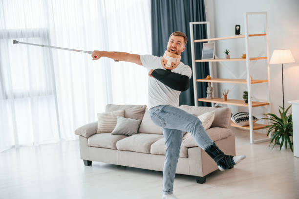 istock Standing, holding crutch in hand and having fun. Man at home indoors. Having injuries 1457976830