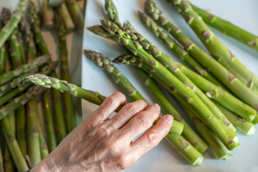 Directly above female hands breaking fresh raw green asparagus on plate