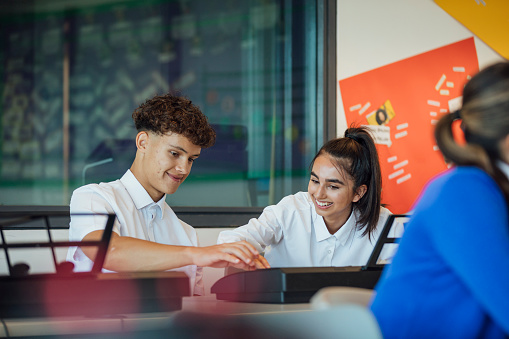 A shot of teenage music students in a classroom learning how to play the keyboard together at a school. The students are wearing school uniforms.