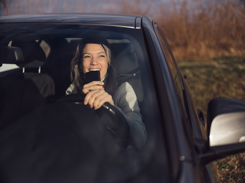 Young happy woman using speech recognition on mobile phone while driving a car. The view is through windshield. Photographed in medium format.
