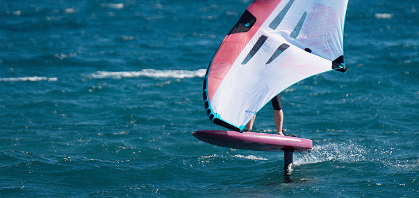 A man is wing foiling using handheld inflatable wings and hydrofoil surfboards in a blue ocean, rider on a wind wing board, surf the waves