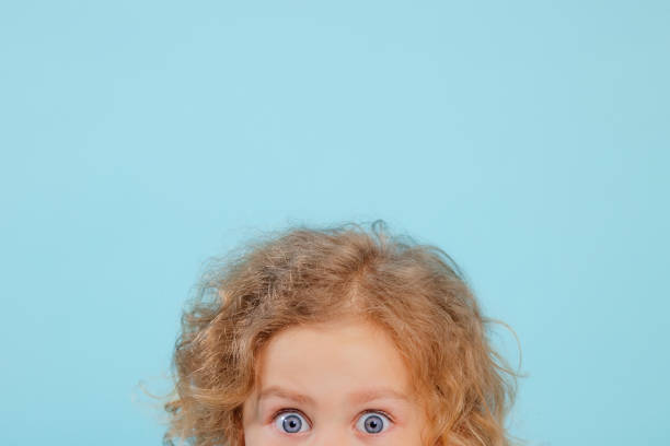 cropped small little expressive, shocked, curious curly blonde girl in pink shirt posing, staring at camera on blue view - surprise child little girls shock imagens e fotografias de stock