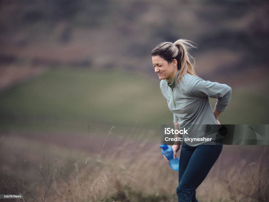 Ugh, my back hurt a lot! Displeased female athlete holding her back in pain during autumn day on a hill. Photographed in medium format. Copy space. Pain Stock Photo