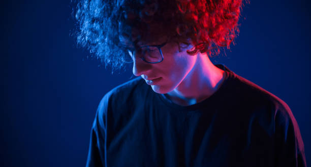 istock Looking down. Young man with curly hair is indoors illuminated by neon lighting 1457980458