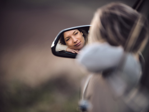 Reflection in a rear-view mirror of relaxed woman day dreaming in a car. Photographed in medium format. Copy space.