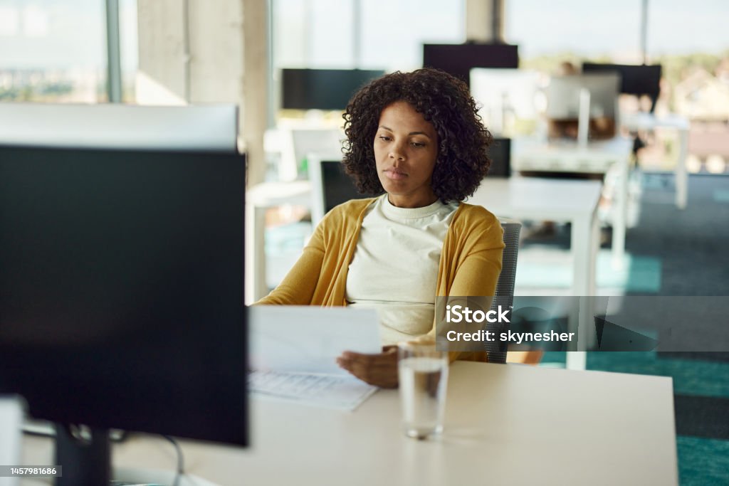 Black businesswoman analyzing reports while working in the office. Young African American female programmer going through paperwork while working in the office. One Woman Only Stock Photo