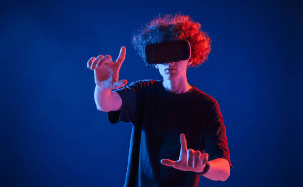 istock Virtual reality experience. Young man with curly hair is indoors illuminated by neon lighting 1457981998