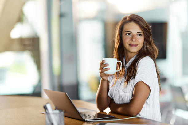 istock Smiling businesswoman day dreaming while drinking coffee in the office. 1457982453