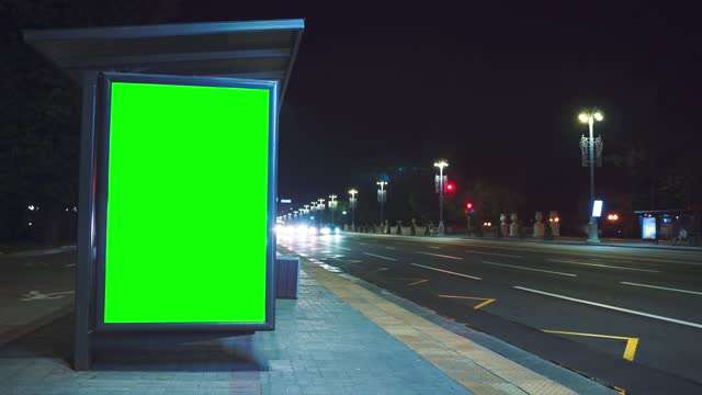 Billboard with chroma key on the street at night and time lapse movement of people and cars in the background.