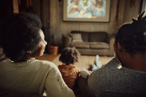 Happy black woman and her family watching a movie on projection screen in the living room.