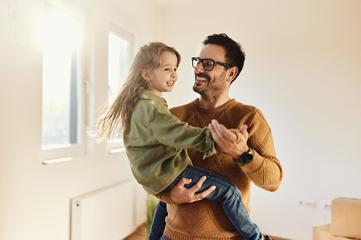 Happy single father having fun while dancing with his small daughter after moving into a new apartment. Copy space.