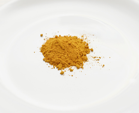 Closeup of a heap of tumeric on a white dinner plate.