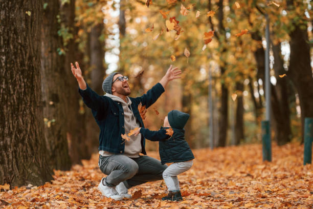 Playing with fallen leaves. Father and young son is together outdoors at daytime.