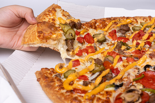 a person taking a slice of pizza from a box with cheese, peppers, mushrooms, and other toppings