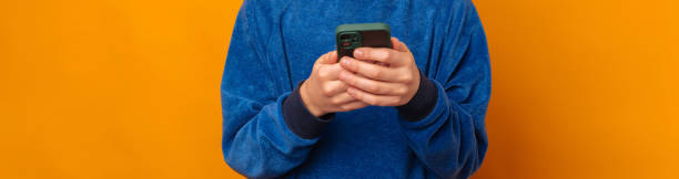 Crop banner size faceless photo of some male kid hands using a smart phone. stock photo