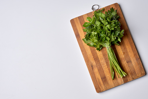 some greens on a wooden cutting board with a knife in the background and a white wall to the left side