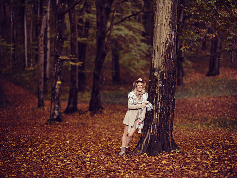 Young happy woman standing among trees during autumn day in the forest and looking at camera. Copy space. Photographed in medium format.