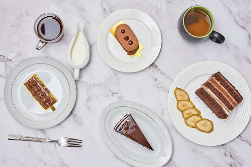 some desserts and coffee on a marble table with white plates, silver spoons, and two different kinds of cakes
