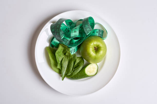 an apple and measuring tape on a white plate with green apples in the top right half, next to it