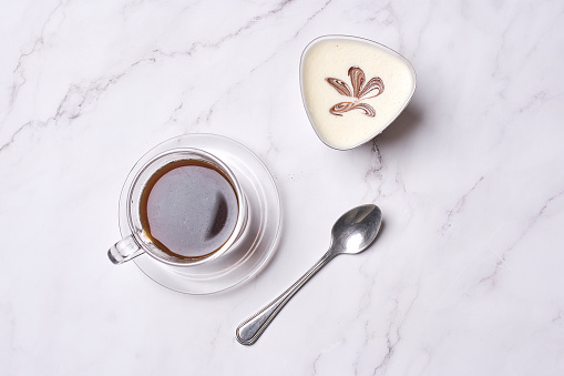 a cup of coffee and spoon on a white marble table with a leaf drawn in the top right hand side