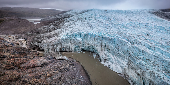 aerial view of melting ice cap creating a river, waterfalls and a tunnel under the ice at Russell Glacier in a cloudy day, Greenland. Russell Glacieris a glacier in the Qeqqata municipality in central-western Greenland. It flows from the Greenland ice sheet (Greenlandic: Sermersuaq) in the western direction. The front of the glacier is located 25 km (16 mi) east of Kangerlussuaq. It is active, advancing 25 m (82 ft) every year,[1] and, due to easy access from Kangerlussuaq, it remains a popular place for tourists to visit.