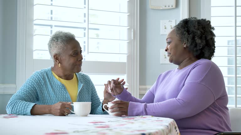 Woman greets senior mother with hug, having tea together