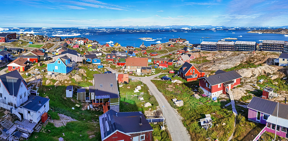 panoramic aerial view of Ilulissat village with icebergs floating in the background. Greenland