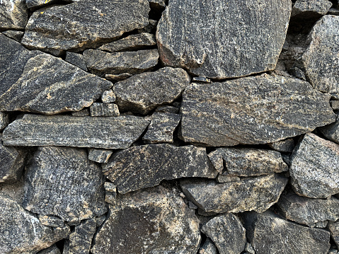 Stock photo showing an irregular dry stone wall, which is providing an attractive boundary. The wall is made from a mixture of stone blocks, which are different sizes and shapes, making it appear more natural and informal in its appearance, particularly as it is now weathered.