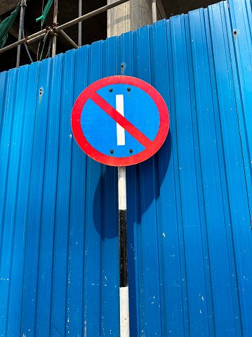 Stock photo showing close-up view of road sign for parking is prohibited on odd days of the month placed in front of blue corrugated metal wall construction site barrier.