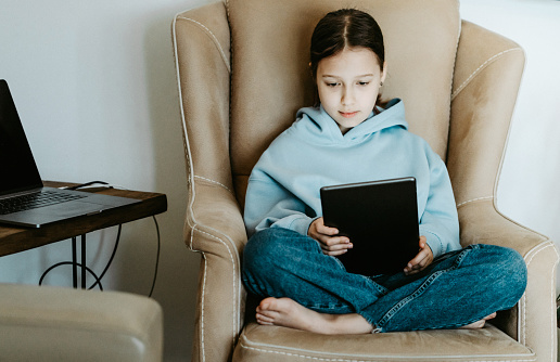 Girl using digital tablet sitting in cozy armchair in living room