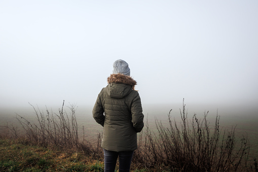 Lost female person in fog. Lonely woman standing in empty misty landscape