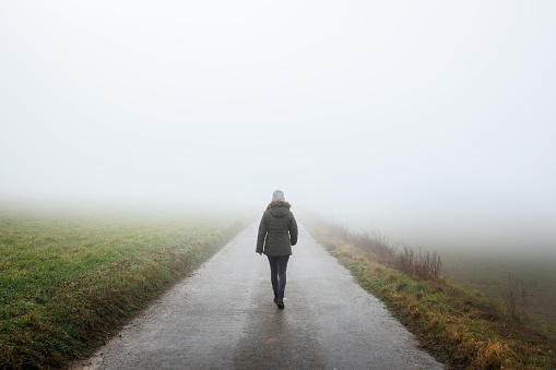 Lonely woman walks on empty road in fog