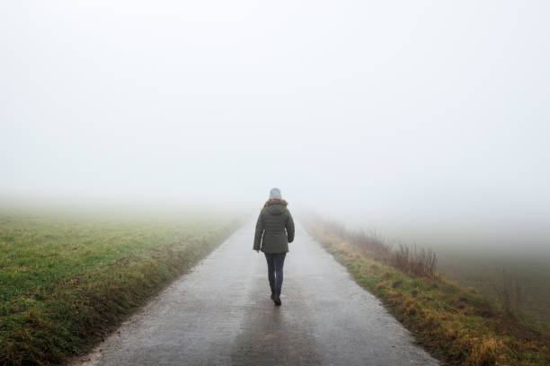 Lonely woman walks on empty road in fog stock photo