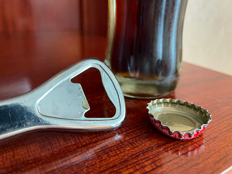 Stock photo showing close-up view of restaurant table setting with glass bottle of coke besides removed metal bottle cap and bottle opener.