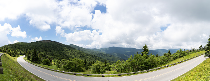Panoramic view at the bend of a winding mountain roadway with a scenic vista beyond, transportation background with creative copy space, horizontal aspect