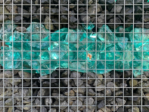 Close-up detail of gabion fence with metal cage filled by crushed stone and shattered artificial blue glass rocks