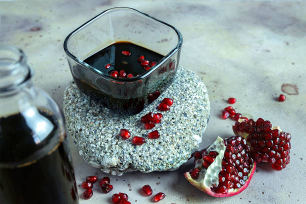 Natural organic pomegranate sause in glass cup on the stone stand. Cut pomegranate fruit and grains on gray background and blurred bottle on foreground. Selective focus. Blurred background. Natural organic pomegranate sause in glass cup on the stone stand. Ripe cut pomegranate fruit and grains on gray background and blurred bottle on foreground. Selective focus. Blurred background. sour taste stock pictures, royalty-free photos & images